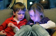Two kids sitting on a sofa playing with an iPad