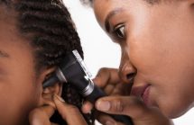 African American doctor looking into the ears of a young girl. Antibiotics are often prescribed for ear infections. Some times needlessly. This is part of the reason we have an antibiotic epidemic.