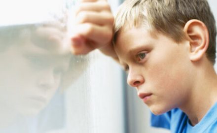 School age boy looking out a window with a pained look on his face.