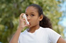 Young African American girl outdoors using an asthma inhaler.