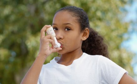 Young African American girl outdoors using an asthma inhaler.