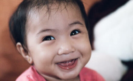 Asian infant with big smile showing baby teeth.