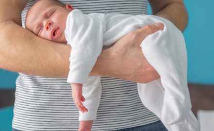 Baby sleeping on his father's arm and hand, in a position to help colic.