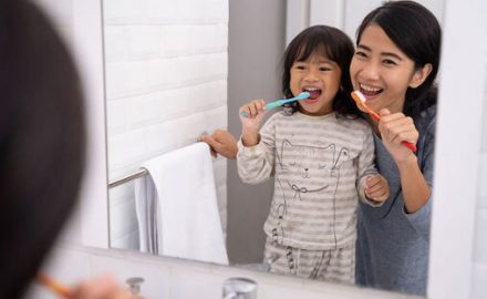 Little Asian girl brushing her teeth with her mother's help. Good dental hygiene is part of bad breath treatment.