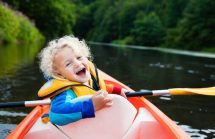 Toddler in a kayak on a beautiful river. He's wearing a life jacket for boating safety.