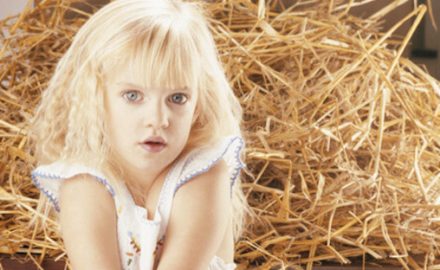 Young blond girl sitting on hay. Could she have celiac disease?