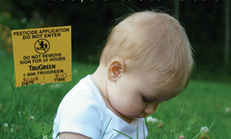 Child sitting on a green lawn with a pesticide warning sign in the background