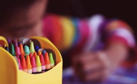 Child coloring using a box of colorful crayons. A child who is color blind may not be able to tell the difference in colors, especially red and green,