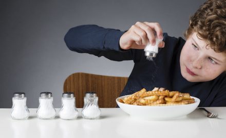 Young boy adding salt to a plate of french fries.