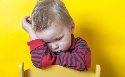 Frustrated toddler standing in front of a yellow wall. Developmental slowdowns can be tough on kids and parents.