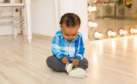Small African american boy playing with his hands and feet. Hands and feet are impacted by Dupuytren's Contracture.