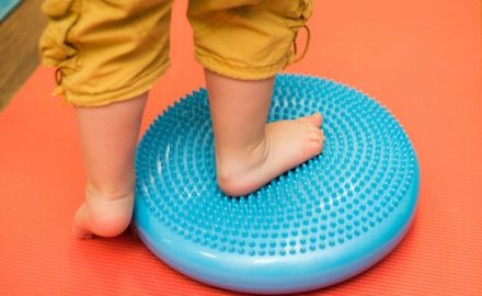 Toddler with flat feet standing on a round saucer with bumps.