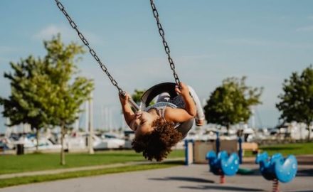 Beautiful black girl swinging on an asphalt playground. Be careful of head injuries.