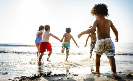 Children playing at the beach in very bright sun. Extreme heat can lead to heat-related illnesses.