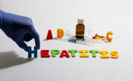 Gloved hand placing letters on a white table that spell out Hepatitis.