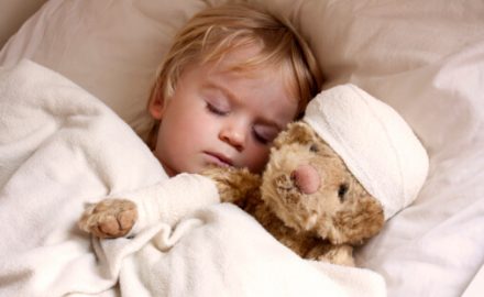 Child laying in bed with a stuffed toy. The toy has a bandage around the nead. Does it need an ice pack or warm compresses?