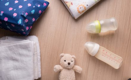 Image of infant and baby gear -- teddy bear, blankets and two bottles. What's the difference between Infant vs. toddler formula?