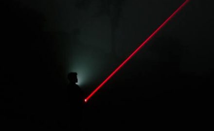 Backlit image of a teenager with a red laser pointers.