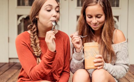 Two teenage girls eating peanut butter out of a jar. Sharing food is a top way mononucleosis is spread.