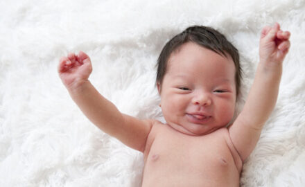 Newborn sounds off in with happy face.