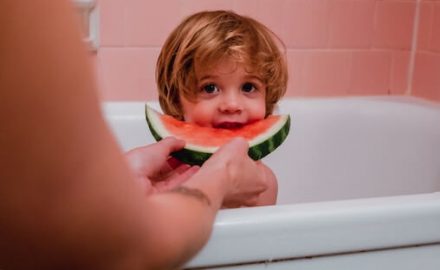 Parent feeding a child watermelon while the child is in a bath. That much be a picky eater! I bet it's Neophobia.