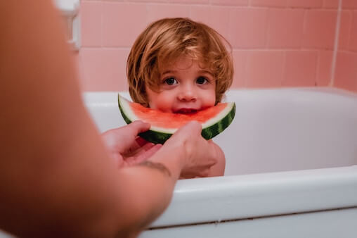 Parent feeding a child watermelon while the child is in a bath. That much be a picky eater! I bet it's Neophobia.