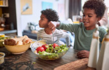 Two African American children eating. One school age, one preschool healthy foods.