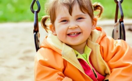 Child playing on a swing in a jacket. This happy child does not have a Rotavirus Virus.