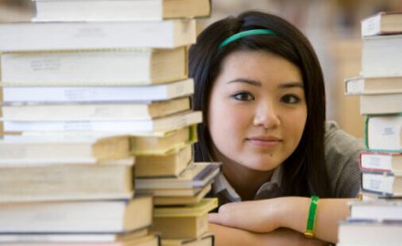 Teenage girl looking through a stack of books. Does she have Scoliosis?