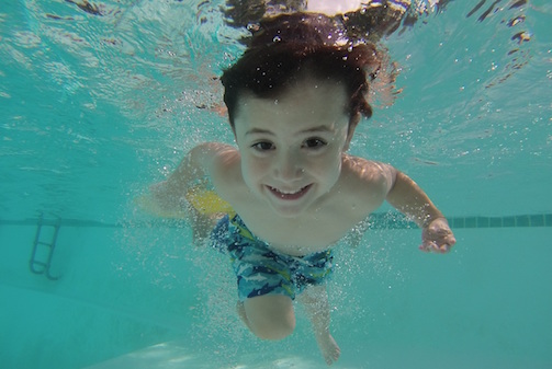 Young boy swimming in a pool with eyes open. Swimming pool water quality.