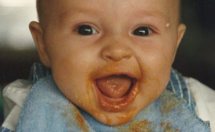 Baby eating carrot puree with huge smile. Timing starting solids is key.