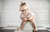 Toddler with big glasses sitting on a potty.