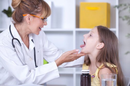 Padriatric docotr looking into the mouth of school girl, treating tonsil stones.