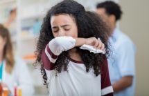 Teen girl with linguring cough at a pharmacy, coughing into her elbow.