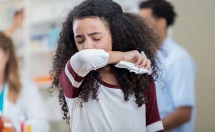 Teen girl with linguring cough at a pharmacy, coughing into her elbow.